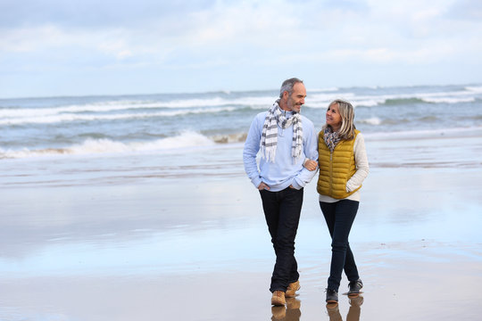 Senior Couple Walking On The Beach In Winter Time