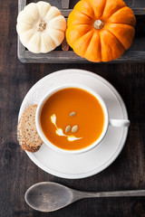 Pumpkin soup with pumpkin seeds in a white cup and raw pumpkins