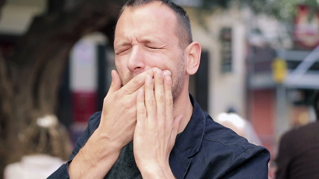 Man having toothache while drinking hot coffee in city