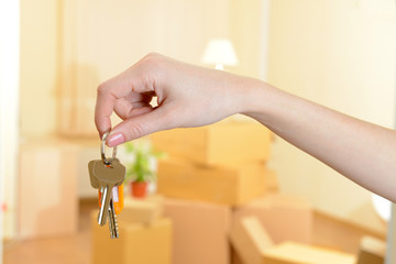 Female hand with keys ob stack of cartons background: moving