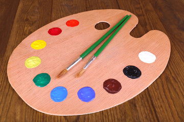 Wooden art palette with paint and brushes on table close-up