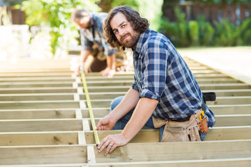 Carpenter Measuring Wood With Tape While Coworker Assisting Him
