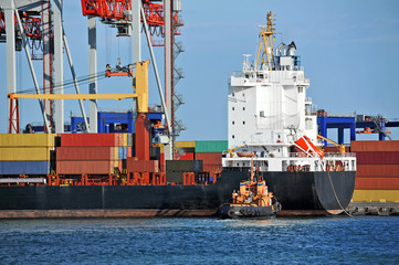 Tugboat assisting container cargo ship to harbor quayside