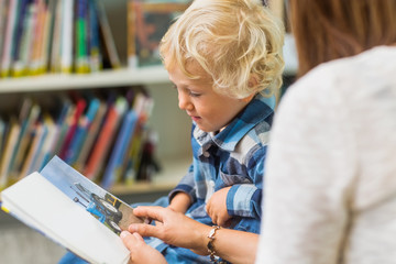 Boy With Teacher Looking At Book In Library