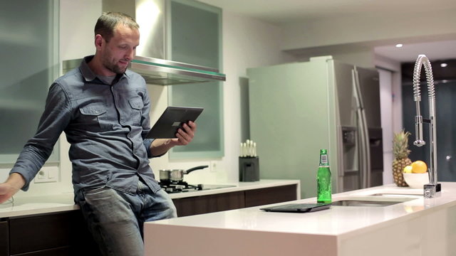 Young man chatting on tablet computer in kitchen