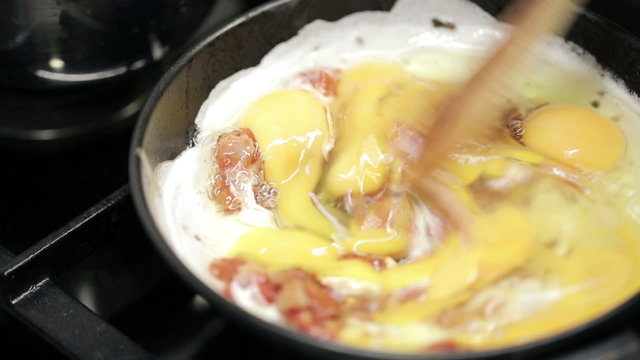 Mixing scrambled eggs on frying pan with wooden spoon