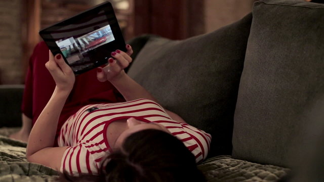 Young woman watching photos on tablet computer on sofa