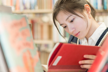 Student reading a book on bookshelf
