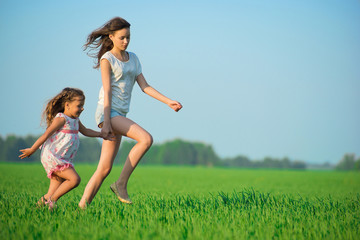 Young happy girls running at green wheat field
