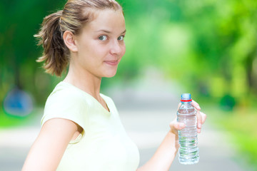 Woman drinking cold mineral water from a bottle after fitness ex