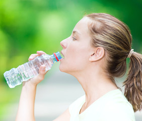 Woman drinking cold mineral water from a bottle after fitness ex
