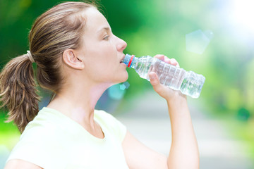 Woman drinking cold mineral water from a bottle after fitness ex