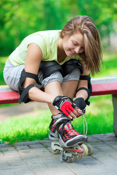 Girl going rollerblading sitting in bench putting on inline skat