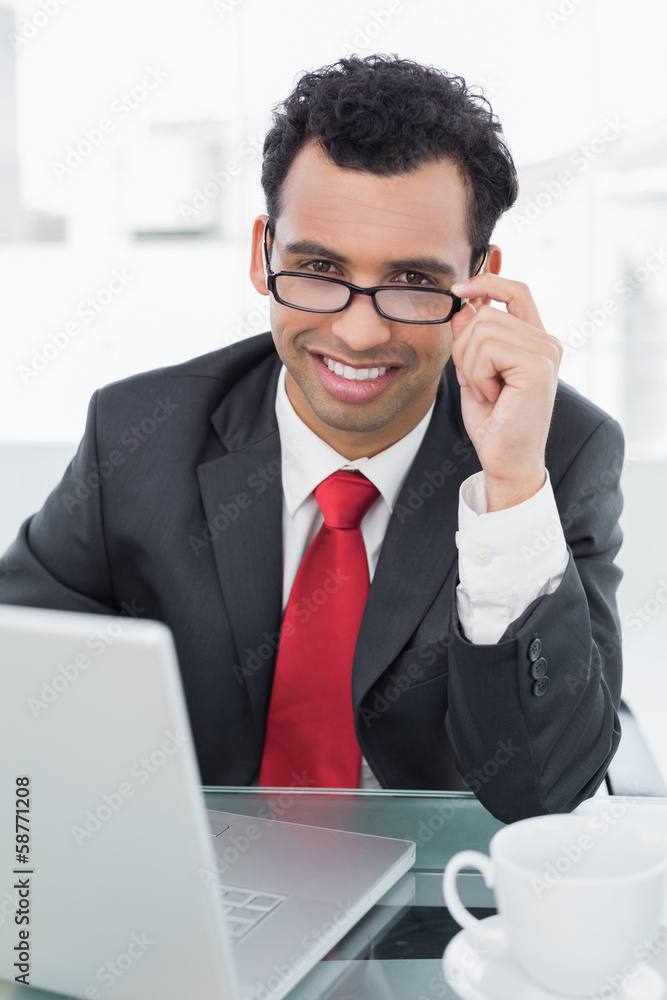 Wall mural Smiling businessman with laptop sitting at office desk