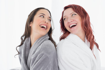 Happy female friends in bathrobes standing back to back