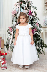 girl in a beautiful white dress stands near a Christmas fir-tree