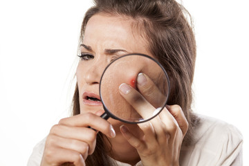 girl squeezing her pimples using magnifying glass