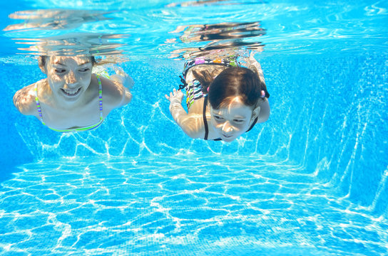 Happy girls swim underwater in pool and having fun