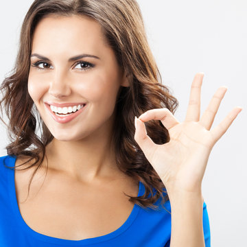 Young woman showing okay gesture, over grey