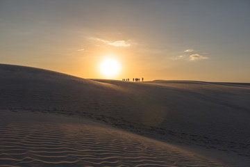Fototapeta na wymiar Travelers walking over sand dunes at sunset