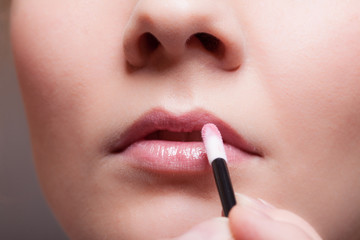 Naklejka premium Makeup. Girl applying lipgloss lipstick on lips. Part of face.