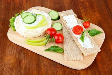 Tasty crispbreads with vegetables on wooden background