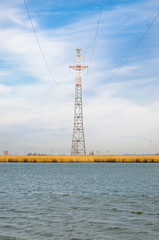 Fototapeta premium Высокая опора линии электропередачи стоит на берегу широкой реки