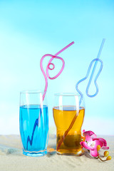 Glasses of cocktails on sand, on bright background