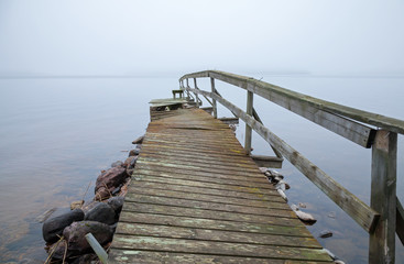 Obraz premium Stary uszkodzony drewniany molo perspektywa nad jeziorem w mglisty poranek