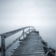 Old ruined wooden pier perspective on the lake in foggy morning