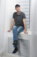 young smiling man sitting on a white window