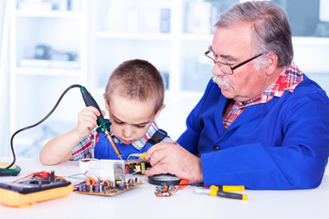 Grandfather teaching grandchild working with soldering iron
