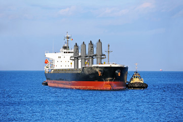 Tugboat assisting bulk cargo ship to harbor quayside