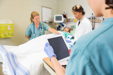 Nurse Holding Digital Tablet While Doctor And Colleague Treating