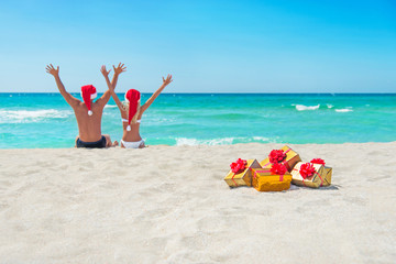 happy couple in santa hats hands up at sea beach with christmas