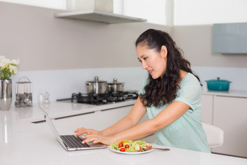 Young woman using laptop while having salad in kitchen