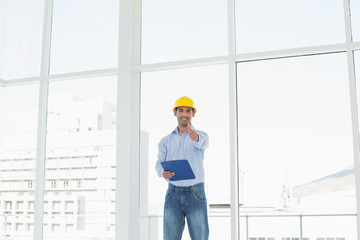 Architect in hard hat with clipboard gesturing thumbs up in offi