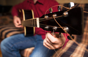 a man sitting on the couch and tuning a guitar