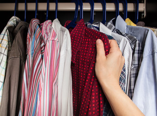 person chooses shirt in the closet of the multi-colored shirts