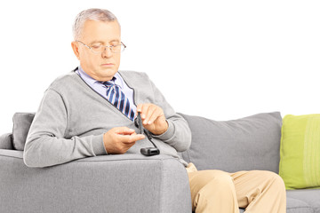 Mature seated on a sofa measuring sugar level in blood