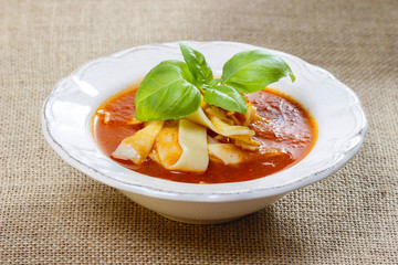 Tomato and pepper soup in white plate on jute table cloth