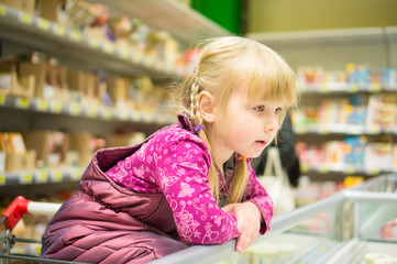 Adorable girl select products at fridge in supermarket