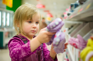 Adorable girl select winter gloves in supermarket