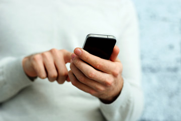 Closeup image of a male hand holding smartphone and typing on it