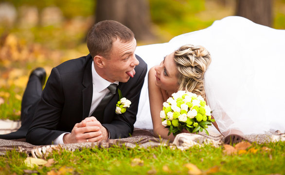 Bride And Groom Lying On Grass At Park And Making Funny Faces