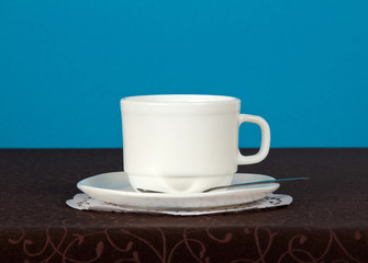 Cup, saucer, spoon, napkin on a brown cloth