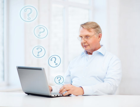 old man in eyeglasses working with laptop at home