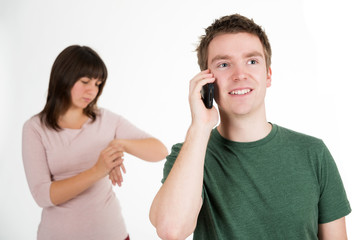 Lachender Mann mit Handy, Frau genervt im Hintergrund