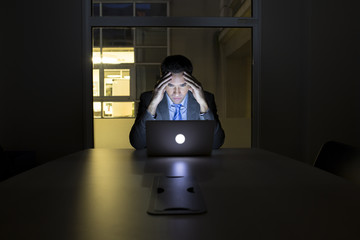 Businessman working late in his office on laptop, night light