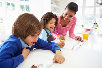 Mother Helping Children With Homework In Kitchen